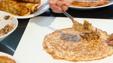 İnsan kaşığı mantar ve et ince ev yapımı krepe doluyor ve katlamaya başlıyor. Bir yığın krep, krep servisi.