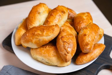 Taze pişmiş lezzetli çörekler, ahşap masanın üzerinde beyaz tabağa istiflenmiş, yumuşak hamur ve dolguyu gösteren, ev yapımı fırın ürünleri.