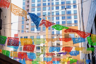 Renkli picado afişleri New York sokaklarındaki şehir binaları arasında asılı, neşeli atmosfer ve canlı şehir sokak dekoru yaratıyor.