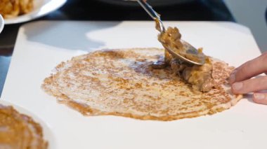 Mutfak tezgahında pişirme hazırlıkları sırasında mantarların ince kreplere dolup yayılması ve katlanması.