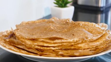 Bir tabakta servis edilen ince altın krep yığınına yakınlaş, ev yapımı kahvaltı yemekleri ve geleneksel krep sunumunu vurgula