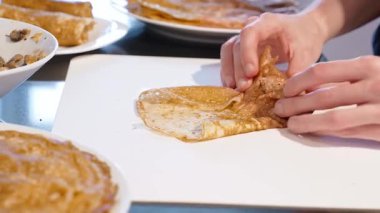 Doldurulmuş krepi kesme tahtasına katlayan ellerin yakın çekimi, ev yapımı krep hazırlama ve servis sürecini gösteriyor