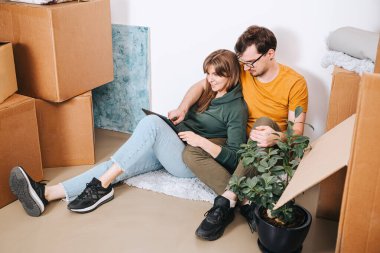 Bir çift taşınan kutuların arasında otururken tablet veya alışveriş mobilyaları sipariş ederken yeni apartman, taşınma, dijital servis