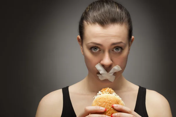 Concepto de dieta: mujer sosteniendo una hamburguesa con boca sellada —  Fotos de Stock