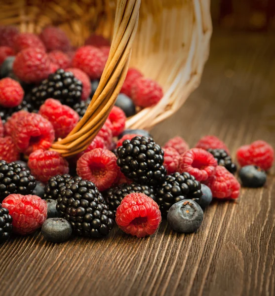 Verschiedene Beeren in einem Korb auf einem Holztisch — Stockfoto