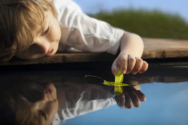 Boy play with leaf ship in water (focus on ship) — Stock Photo, Image