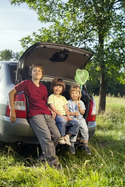 Trois enfants joyeux assis dans le coffre d'une voiture sur la nature — Photo
