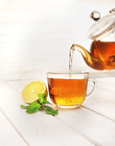 Чашка чая, стеклянный чайник, мята и лимон на деревянном столе — стоковое фото
