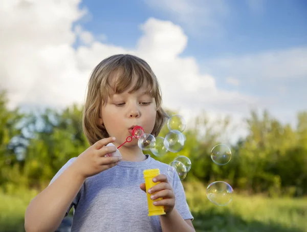 Gelukkige jongen spelen in bubbels buitenshuis — Stockfoto