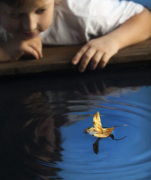 Boy play with leaf ship in water (focus on ship) — Stock Photo, Image