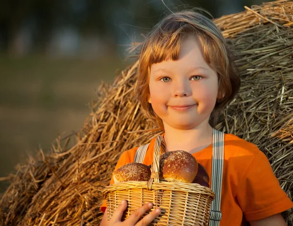 Boy with basket of buns in the background of haystacks in a field — Stock Photo, Image