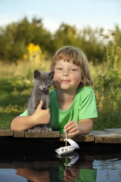 boy and his beloved kitten playing with a boat from pier in pond