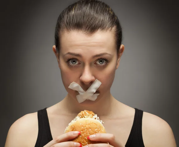 Diet concept: woman holding a burger with mouth sealed Stock Picture