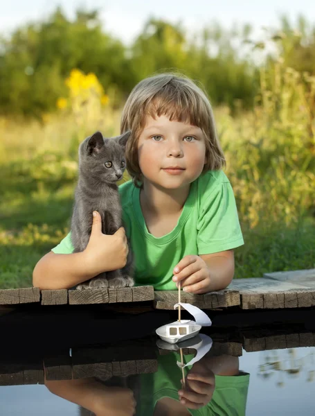 Jongen en zijn geliefde kitten spelen met een boot van pier in vijver — Stockfoto