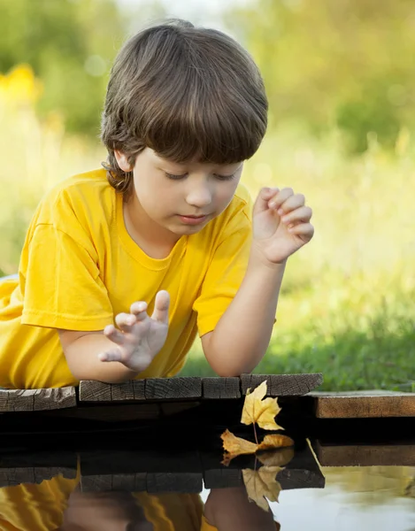 Boy play with autumn leaf ship in water — Stock Photo, Image