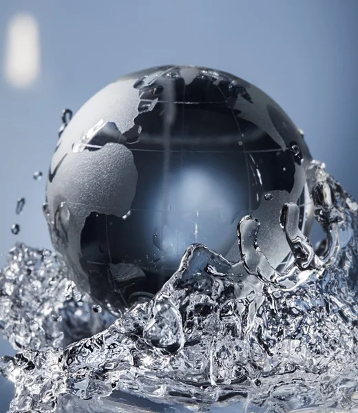 Planeta globo de vidrio en gota salpicadura de agua sobre fondo azul —  Fotos de Stock