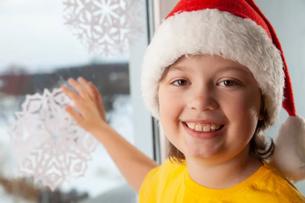 少年は家の中で冬の窓の近くに雪片を突きつけているクリスマス イブの休日の木 — ストック写真