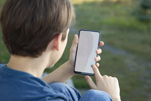 黒のスマートフォンのブランクスクリーンを保持している男の子自然を背景に現代的なフレームレスなデザイン — ストック写真