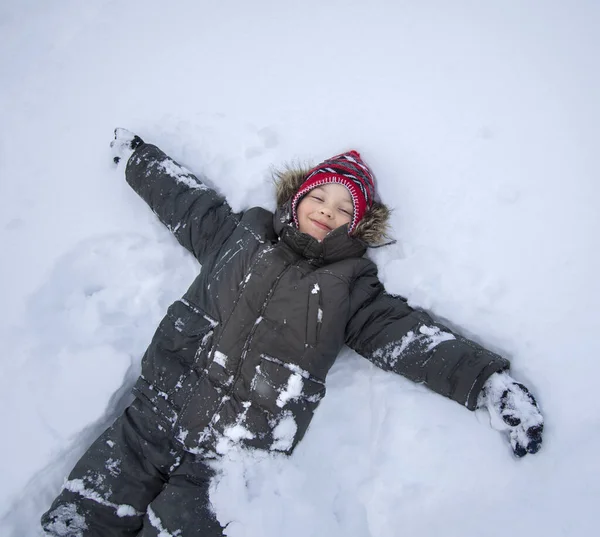 Glücklicher Junge Der Auf Schnee Liegt Und Mit Händen Und — Stockfoto