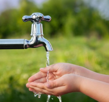 Çocuk elini bahçedeki musluğun altında yıkıyor.