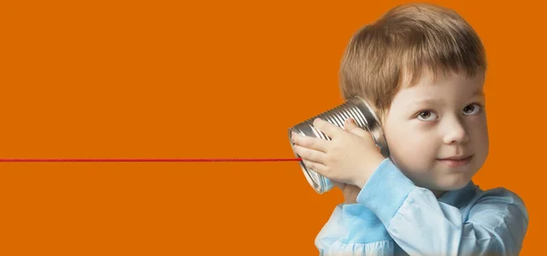 男の子は錫缶電話で遊んでいます オレンジの背景に隔離 — ストック写真