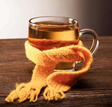 Ahşap arka planda bir eşarp içinde çay bardağı, şifa konsepti.