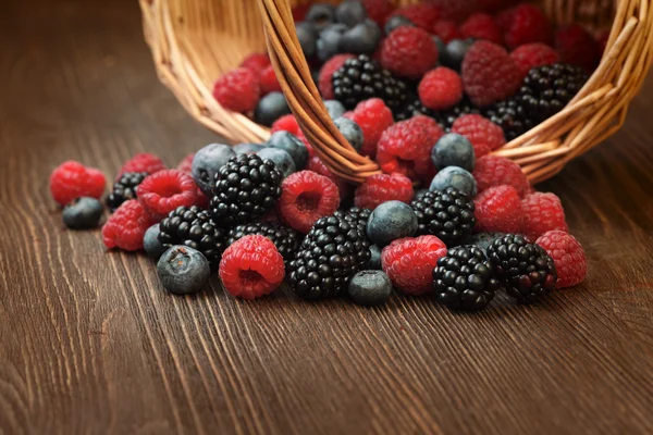 Verschiedene Beeren in einem Korb auf einem Holztisch — Stockfoto