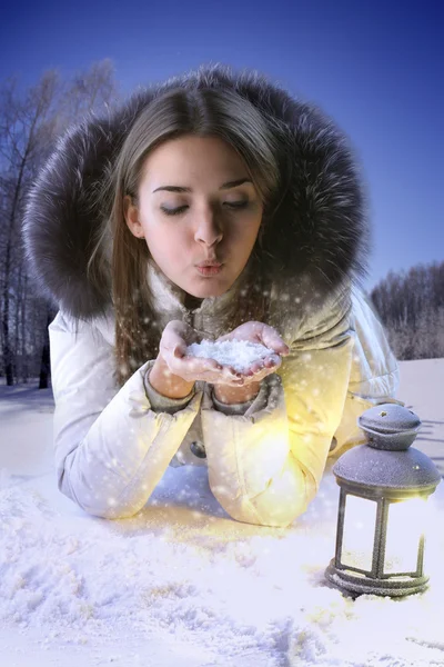 Flicka på en vinter glade blåser på snöflingor. — Stockfoto