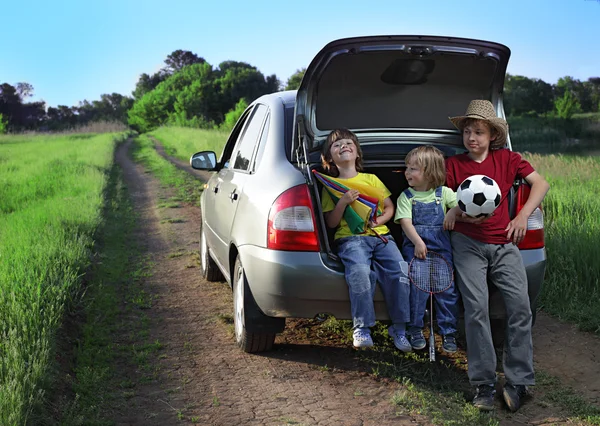Três crianças alegres sentadas no porta-malas de um carro na natureza — Fotografia de Stock