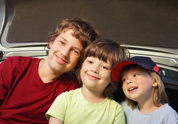 Three cheerful child sitting in the trunk of a car on nature — Stock Photo, Image