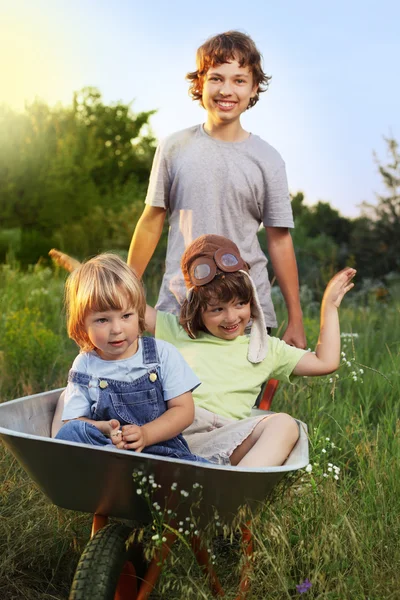 Three brother playing in the plane using a garden carts — Stock Photo, Image