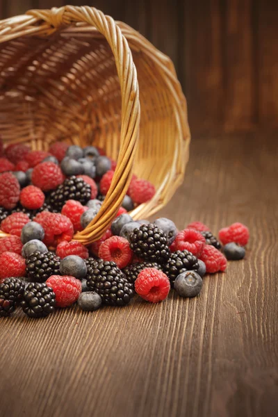 Different berries in a basket on a wooden table — Stock Photo, Image