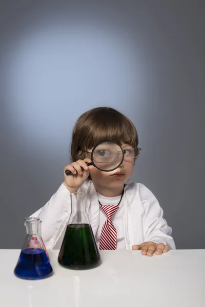 Boy studying a substance in a test tube with a magnifying glass — Stock Photo, Image