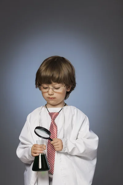 Jongen bestuderen van een stof in een reageerbuis met een vergrootglas — Stockfoto