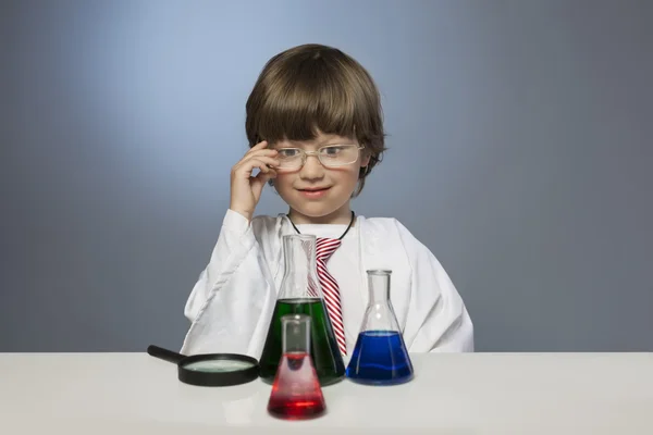 Мальчик изучает вещество в пробирке с лупой — стоковое фото