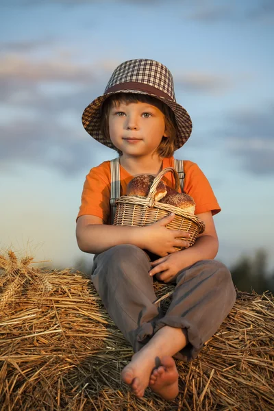 Jongen met mandje voor broodjes in de achtergrond van hooibergen in een veld — Stockfoto