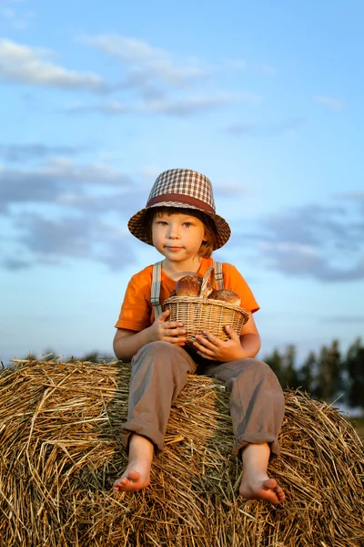 Хлопчик з кошиком з булочок на задньому плані стосів сіна в полі — стокове фото