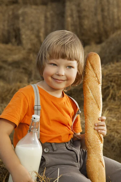 Child on a haystack with bread and milk — Stock Photo, Image