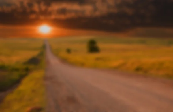 Imagem de fundo borrada do pôr-do-sol dramático sobre a estrada rural — Fotografia de Stock