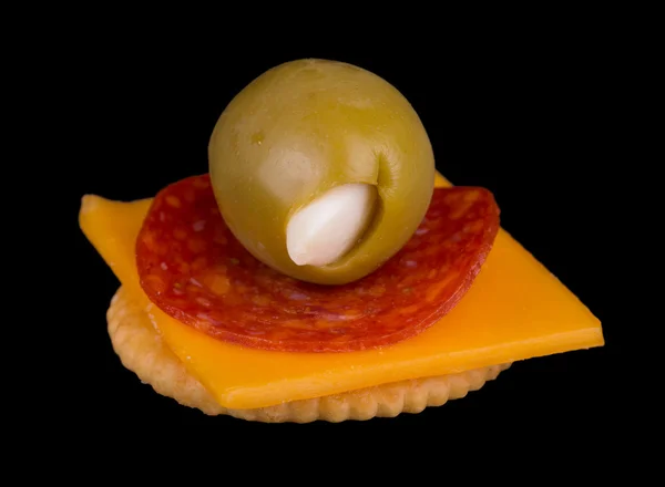 Cracker with cheese, pepperoni and a garlic stuffed olive, isolated on black — Stock Photo, Image