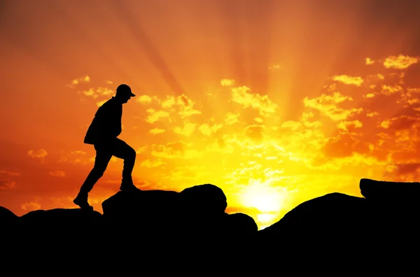 Sziluettjét egy férfi mászni a tetején egy hegy againt napkelte — Stock Fotó
