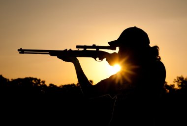 Silhouette of a young man shooting with a long rifle against sunset sky, with a sunburst clipart
