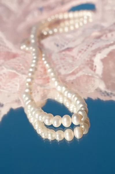 Loop of white natural pearls on pink lace and reflection on blue — Stock Photo, Image