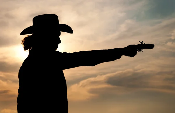 Silhueta de um jovem com um chapéu de cowboy disparando uma arma de mão antiga — Fotografia de Stock