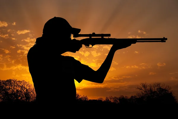 Silhouette eines jungen Mannes, der mit einem Gewehr gegen den dramatischen Himmel schießt — Stockfoto