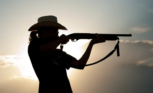 Silueta de un joven en un sombrero de vaquero disparando con una escopeta — Foto de Stock