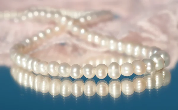 Delicate perle bianche su pizzo rosa, con riflesso — Foto Stock