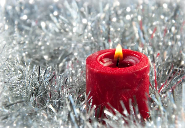 Rote Weihnachtskerze mitten in silbernem Lametta — Stockfoto