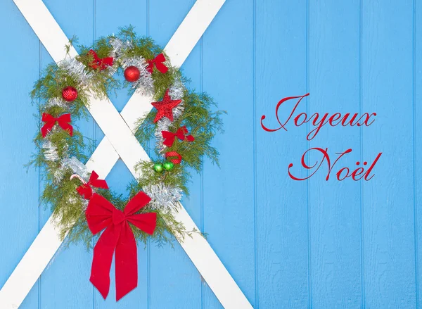 Corona de Navidad colgando en una puerta azul granero con texto Joyeux Noel, Feliz Navidad en francés — Foto de Stock