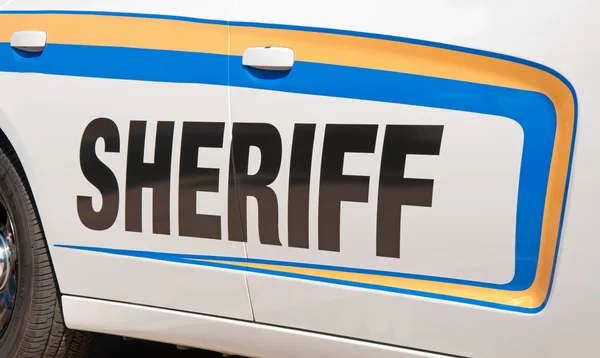 Шериф Текст в черном на стороне белой патрульной машины с желтыми и синими наклейками — стоковое фото